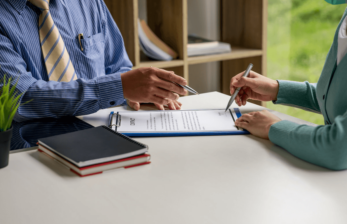 Two people signing an agreement across a desk