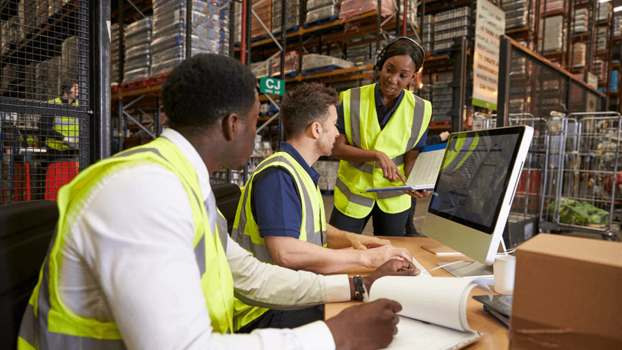 Warehouse colleagues in high-visibility vests reviewing a document together