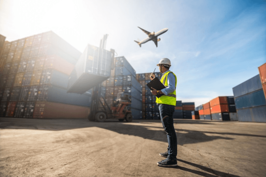 A freight yard worker watching a cargo aircraft climb overhead